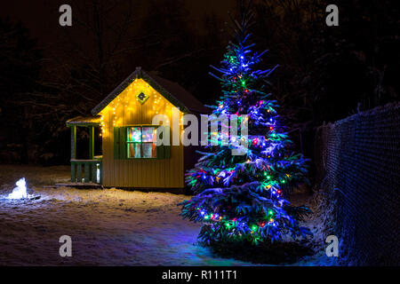 Wooden painted yellow private children`s play house in home garden, decorated with Christmas LED string lights outdoors in cold winder night. Decorate Stock Photo